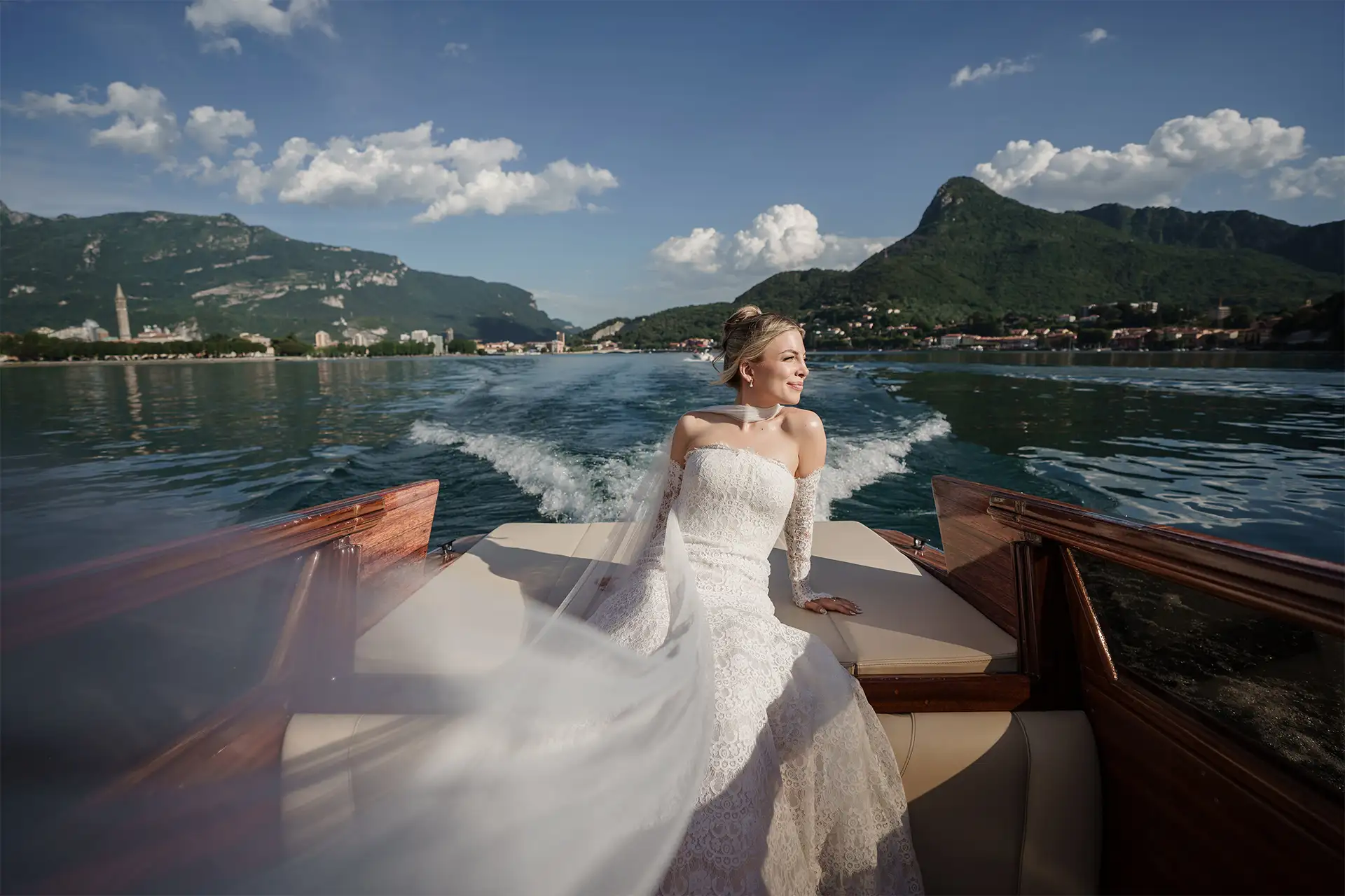 Bride sitting on a wooden boat with the Lake Como landscape behind her