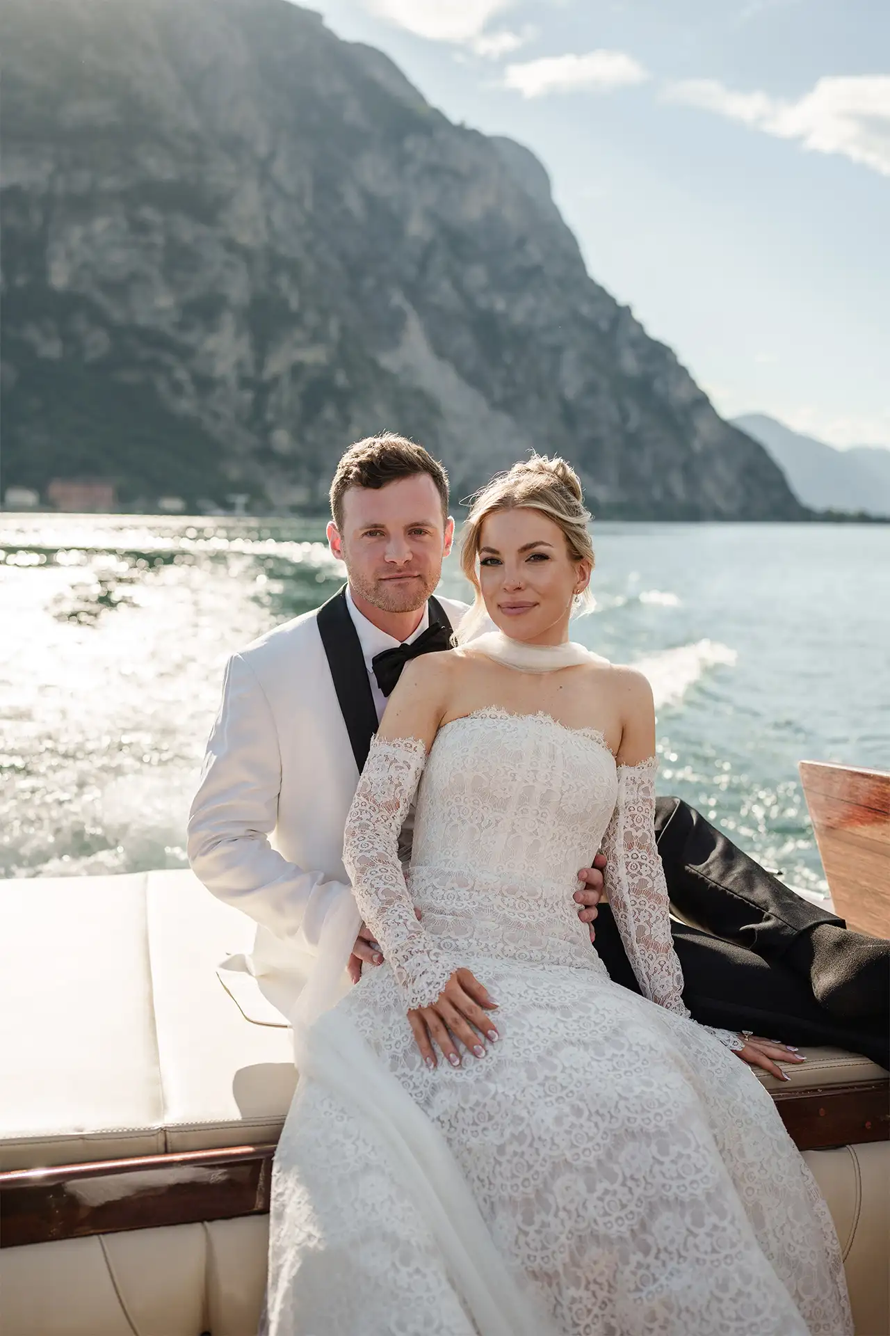 Bride and groom kissing on a wooden boat with Lake Como behind them